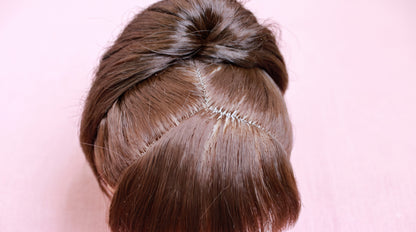 Close-up of a person's hair styled in a messy bun, showing the scalp and hairline stitches, against a solid pink background.